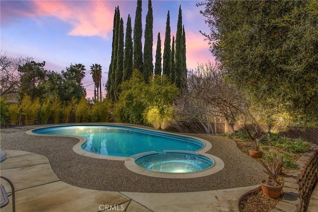 pool at dusk with an in ground hot tub and a patio