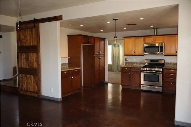 kitchen with a barn door, appliances with stainless steel finishes, hanging light fixtures, and light stone counters