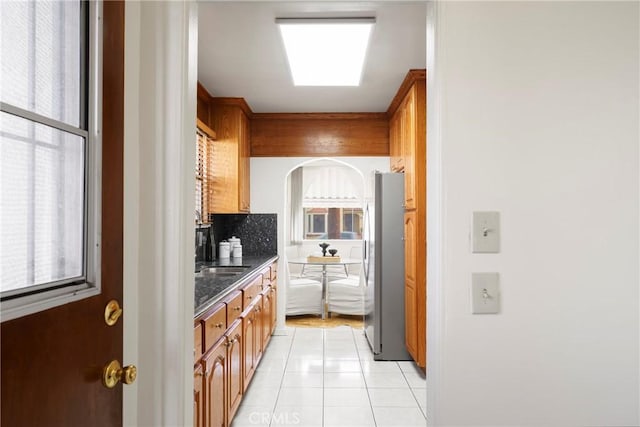 kitchen featuring light tile patterned flooring, dark stone countertops, stainless steel fridge, and backsplash