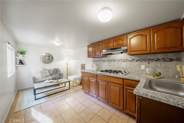 kitchen with sink, gas stovetop, light tile patterned floors, light stone countertops, and decorative backsplash