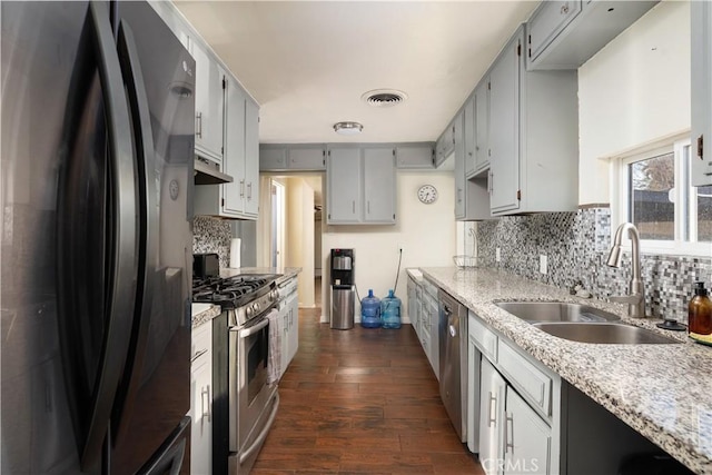 kitchen with sink, dark wood-type flooring, backsplash, stainless steel appliances, and light stone countertops