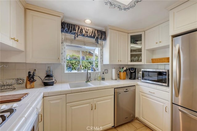 kitchen with appliances with stainless steel finishes, tile counters, sink, and decorative backsplash