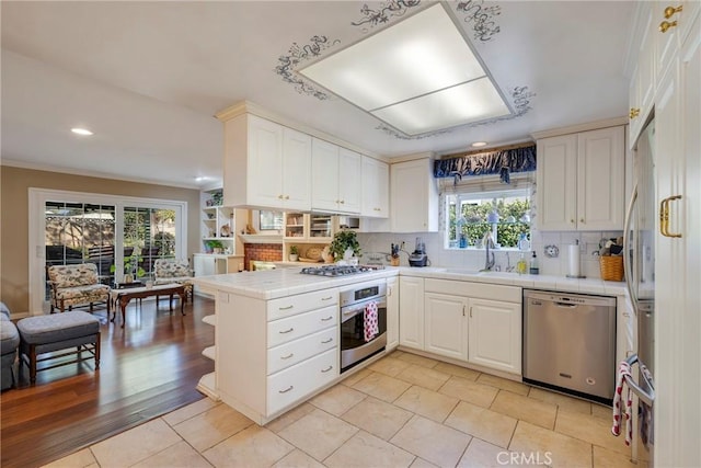 kitchen featuring sink, tile countertops, kitchen peninsula, stainless steel appliances, and white cabinets