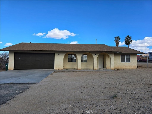 single story home with a garage, driveway, a shingled roof, and stucco siding