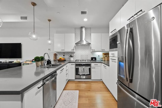 kitchen featuring appliances with stainless steel finishes, sink, white cabinets, hanging light fixtures, and wall chimney exhaust hood