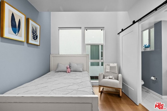 bedroom with a wall unit AC, a barn door, and light wood-type flooring