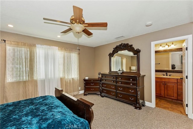 bedroom with ceiling fan, light colored carpet, sink, and ensuite bath