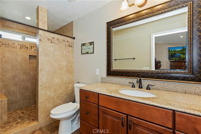 bathroom with vanity, a tile shower, and toilet