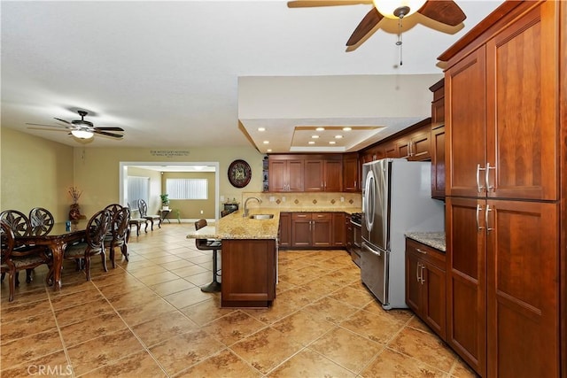 kitchen featuring a breakfast bar, stainless steel refrigerator, sink, decorative backsplash, and light stone countertops