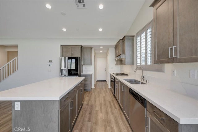 kitchen with stainless steel appliances, a kitchen island, sink, and light hardwood / wood-style floors