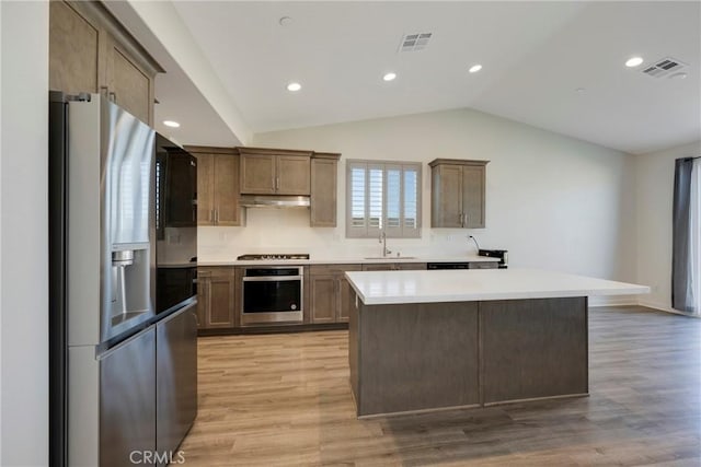 kitchen featuring sink, appliances with stainless steel finishes, a kitchen island, vaulted ceiling, and light wood-type flooring