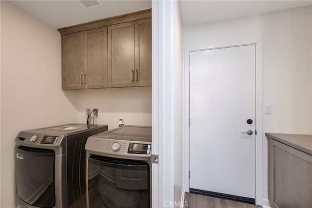 laundry room with cabinets, washing machine and clothes dryer, and light hardwood / wood-style flooring