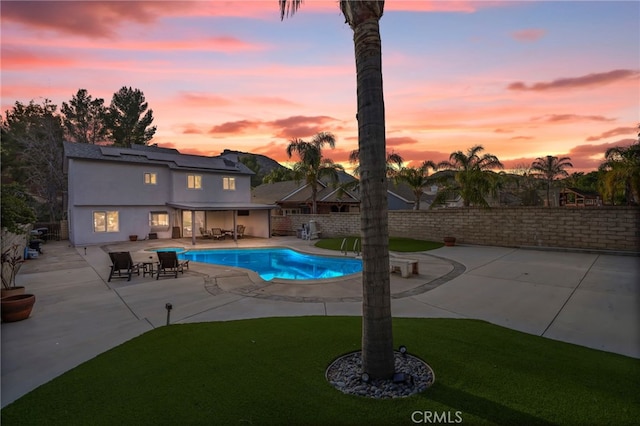 pool at dusk with a yard and a patio area