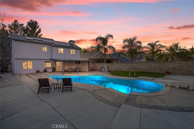 pool at dusk with a hot tub and a patio