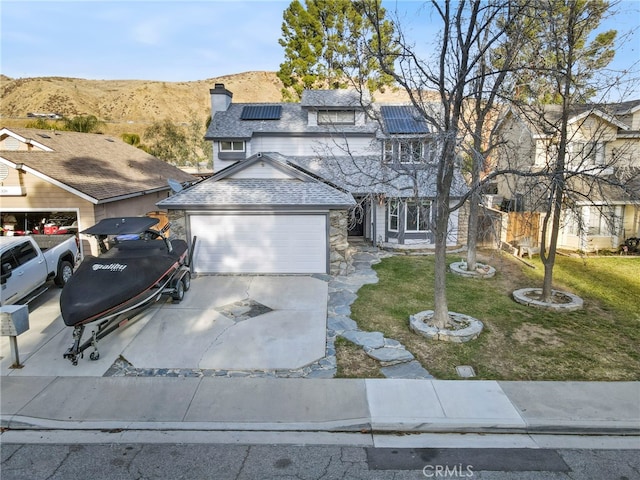 view of front facade featuring a garage, a mountain view, a front yard, and solar panels