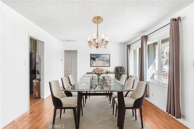 dining room featuring a textured ceiling, a notable chandelier, and light wood-type flooring