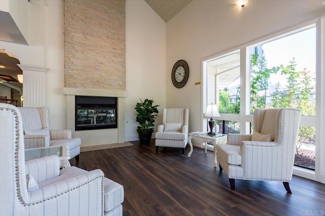 living room featuring a stone fireplace, dark wood-type flooring, high vaulted ceiling, and ornate columns