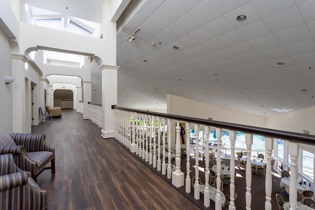 hall featuring dark wood-type flooring, a towering ceiling, and ornate columns