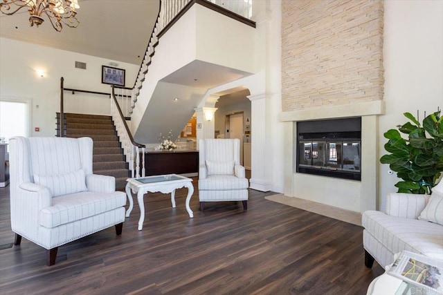 sitting room featuring dark wood-type flooring, a multi sided fireplace, an inviting chandelier, and a towering ceiling