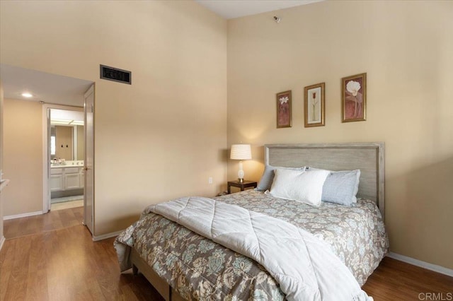 bedroom with a high ceiling, wood-type flooring, and ensuite bathroom