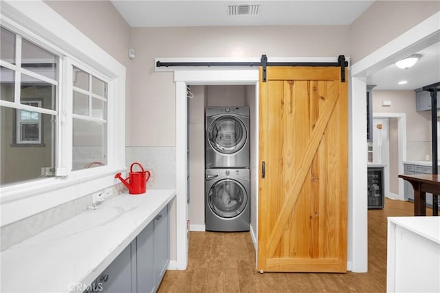 laundry room featuring stacked washer / drying machine, a barn door, beverage cooler, and light hardwood / wood-style flooring