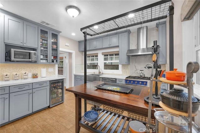 kitchen featuring appliances with stainless steel finishes, decorative light fixtures, sink, wine cooler, and wall chimney range hood