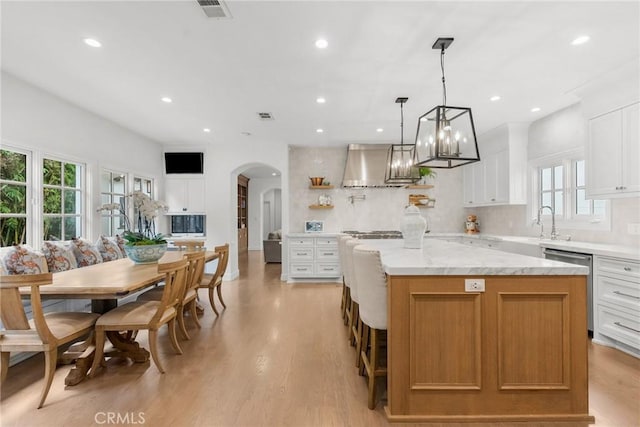 kitchen with a kitchen island, white cabinetry, stainless steel dishwasher, light stone countertops, and wall chimney exhaust hood