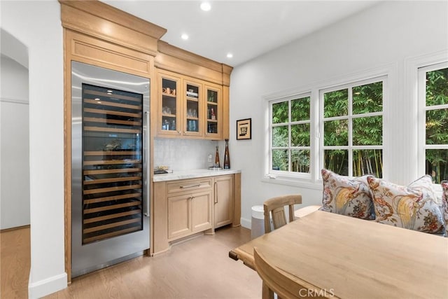 bar with light stone counters, beverage cooler, light brown cabinetry, and light wood-type flooring