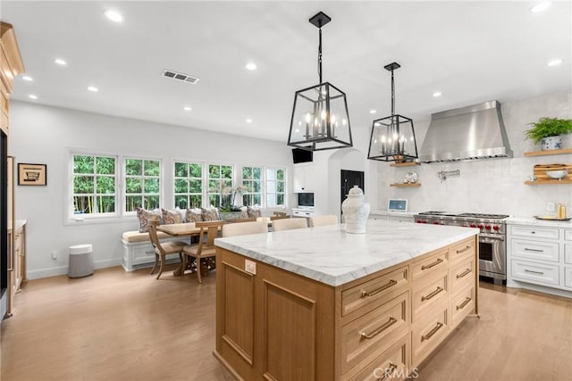 kitchen featuring decorative light fixtures, white cabinetry, high end range, a center island, and wall chimney range hood