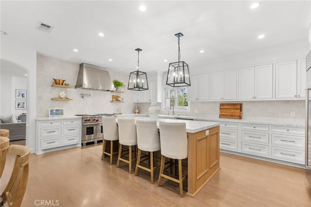 kitchen featuring white cabinetry, double oven range, a kitchen island, and wall chimney exhaust hood