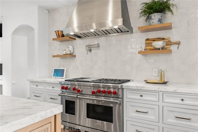 kitchen with premium stove, light stone countertops, white cabinets, island exhaust hood, and decorative backsplash