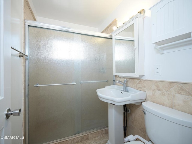 bathroom with a shower with door, tile walls, and toilet