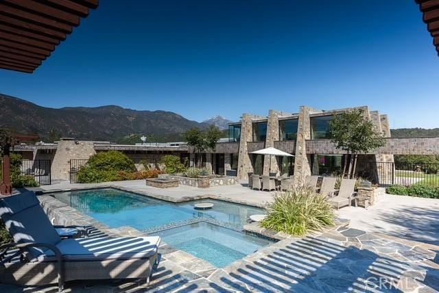 view of pool featuring a patio, a mountain view, a fire pit, fence, and a pool with connected hot tub