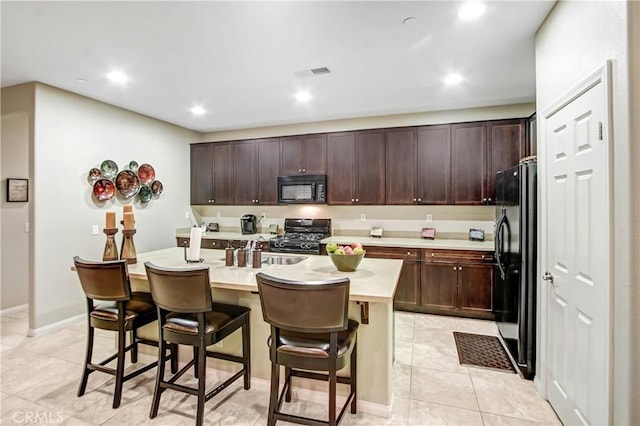 kitchen with dark brown cabinetry, a kitchen bar, a center island with sink, and black appliances