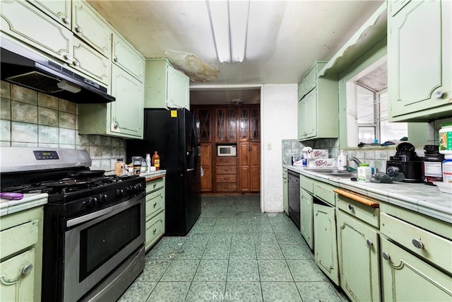 kitchen with sink, tasteful backsplash, tile countertops, green cabinets, and black appliances