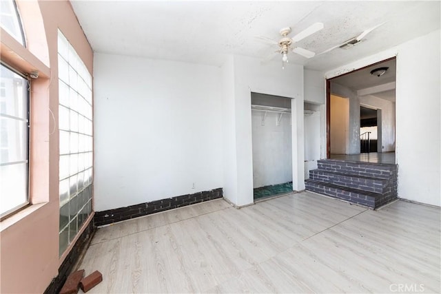 unfurnished bedroom with ceiling fan, a closet, light hardwood / wood-style floors, and multiple windows