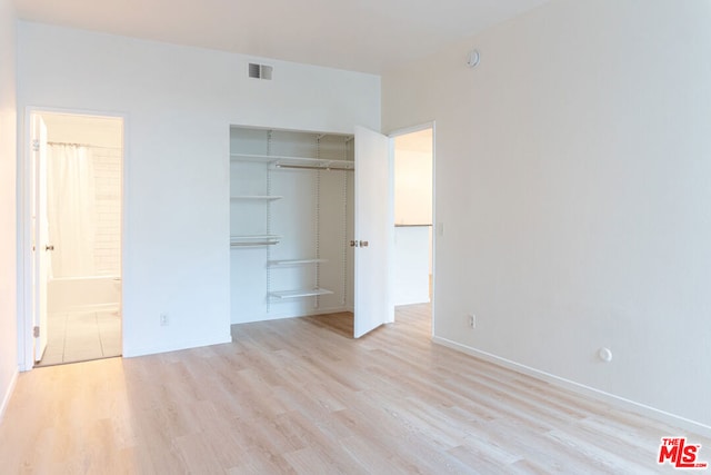 unfurnished bedroom featuring ensuite bath, a closet, and light wood-type flooring