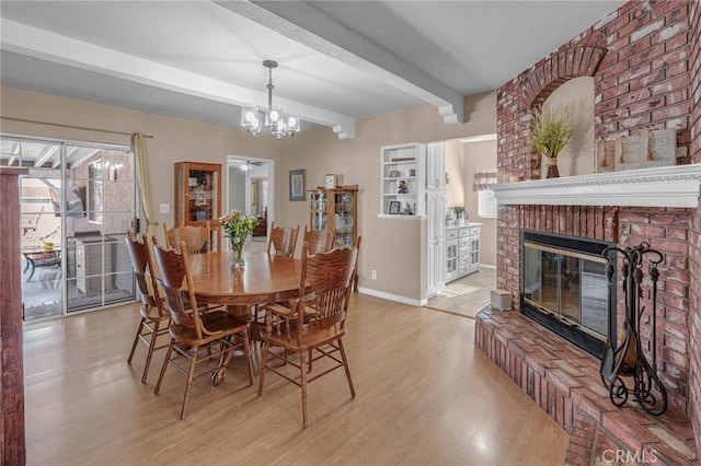 dining area featuring beamed ceiling, a brick fireplace, a notable chandelier, and light hardwood / wood-style floors