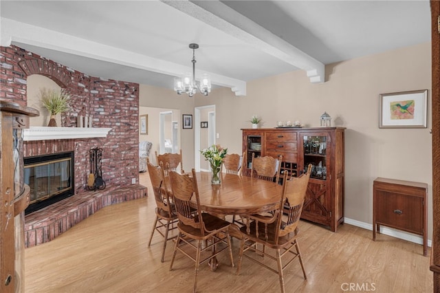 dining space featuring an inviting chandelier, a brick fireplace, beamed ceiling, and light wood-type flooring