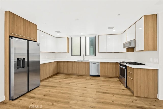 kitchen with white cabinetry, appliances with stainless steel finishes, sink, and light hardwood / wood-style floors