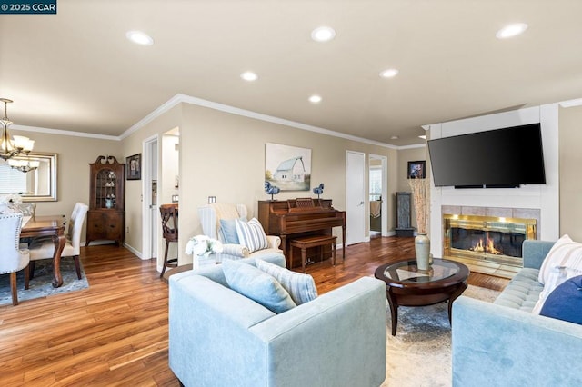 living room with an inviting chandelier, ornamental molding, wood-type flooring, and a fireplace