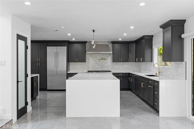 kitchen with sink, a center island, stainless steel built in fridge, decorative light fixtures, and wall chimney exhaust hood