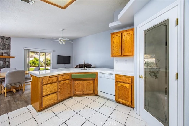 kitchen with tile countertops, vaulted ceiling, light tile patterned floors, dishwasher, and kitchen peninsula