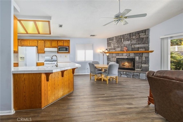 kitchen with lofted ceiling, a stone fireplace, sink, tile countertops, and white appliances