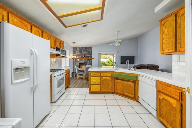 kitchen with light tile patterned flooring, vaulted ceiling, kitchen peninsula, white appliances, and a fireplace