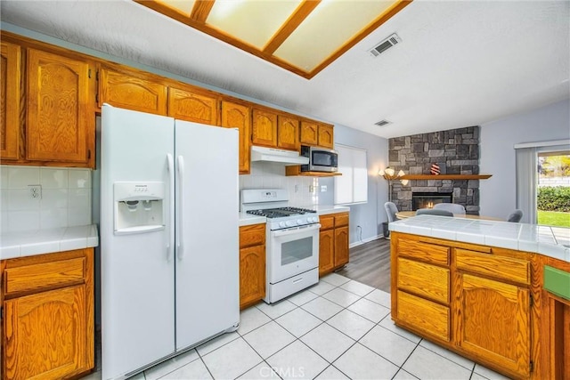 kitchen with a fireplace, tasteful backsplash, tile counters, light tile patterned floors, and white appliances