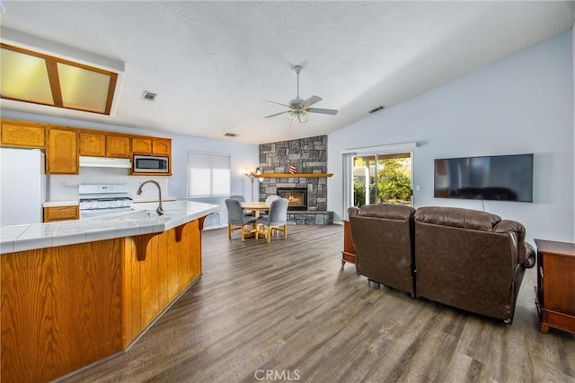 kitchen with lofted ceiling, white appliances, dark wood-type flooring, tile counters, and a stone fireplace