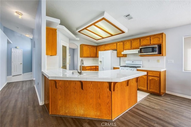 kitchen with white appliances, dark wood-type flooring, a kitchen breakfast bar, tile counters, and kitchen peninsula