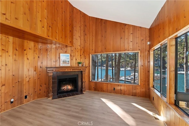 unfurnished living room with a water view, wood walls, a tiled fireplace, and hardwood / wood-style flooring