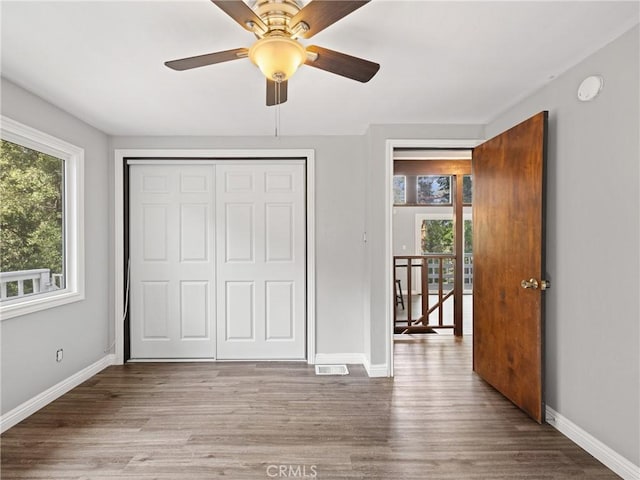 unfurnished bedroom featuring hardwood / wood-style flooring, a closet, ceiling fan, and multiple windows